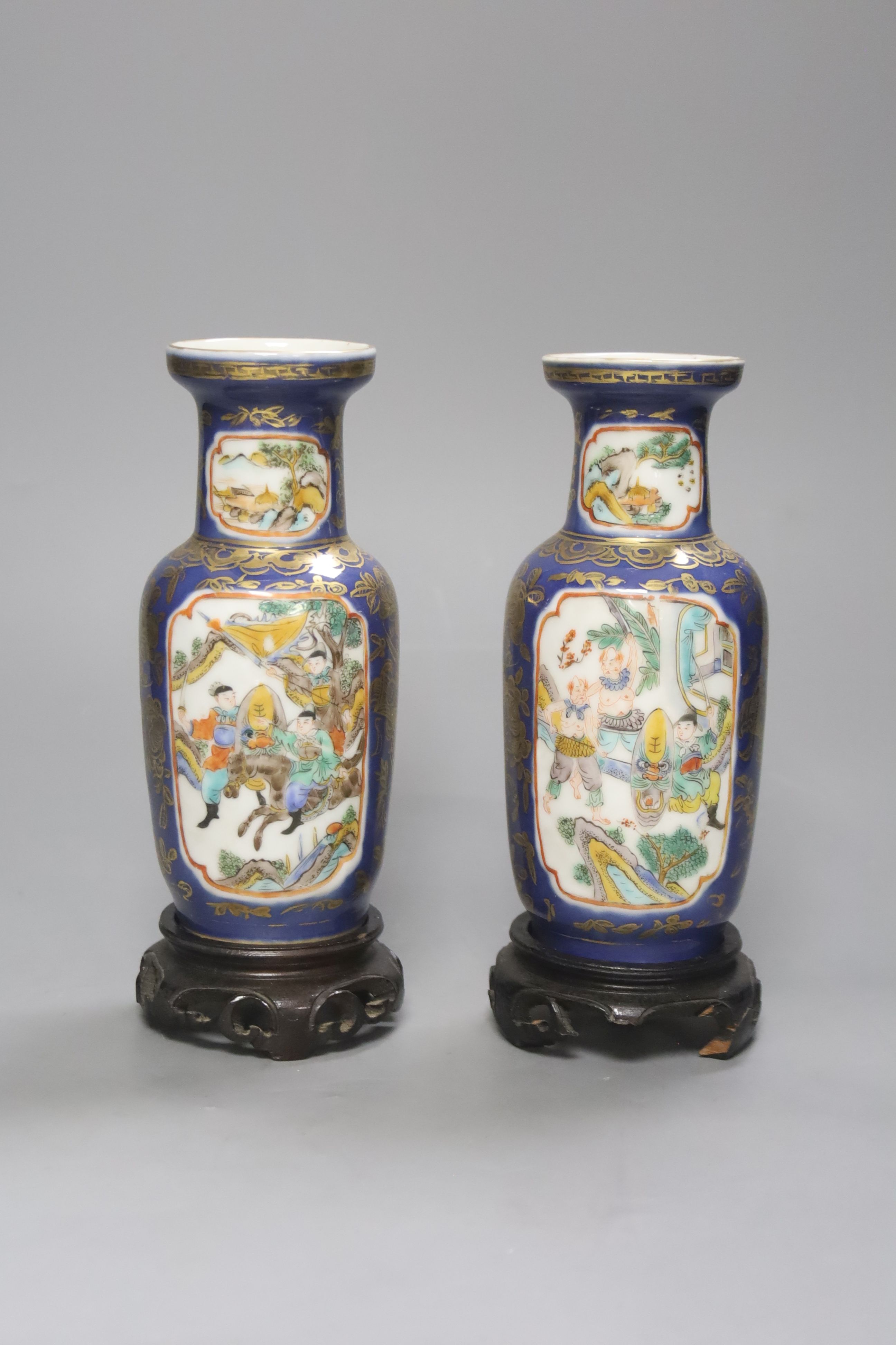 A pair of Chinese Kangxi style blue-ground vases, late 19th century decorated with panels of warriors and heightened in gilt, on carved hardwood stands, height 18cm excluding stand